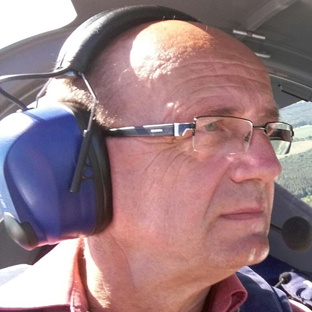 Mann mit Brille und Headset mit Mikrofon im Cockpit eines Leichtflugzeugs, Blick nach vorne gerichtet.
